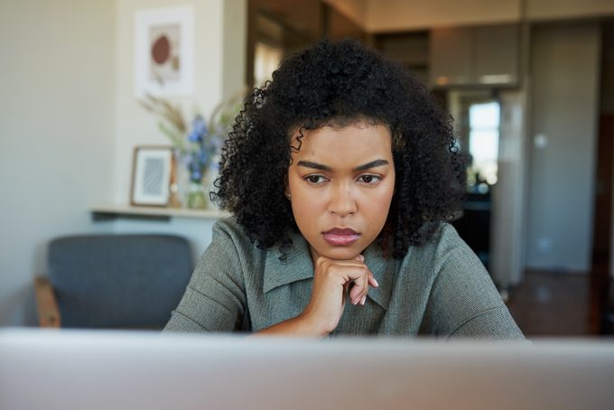 Person intently focuses on a laptop, sitting in a modern home environment with framed pictures and flowers in the background.