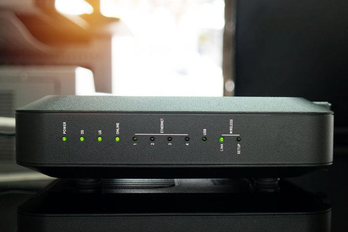 A black router displaying green and amber lights; placed on a black surface in an indoor setting.