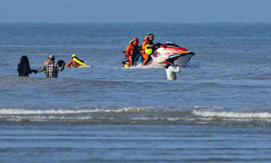 French police on a jetski sail past migrants in shallow water