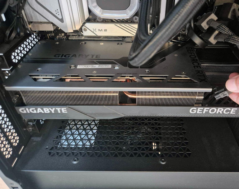 A graphics card sits inside a PC case. Someone is plugging in the power connector.