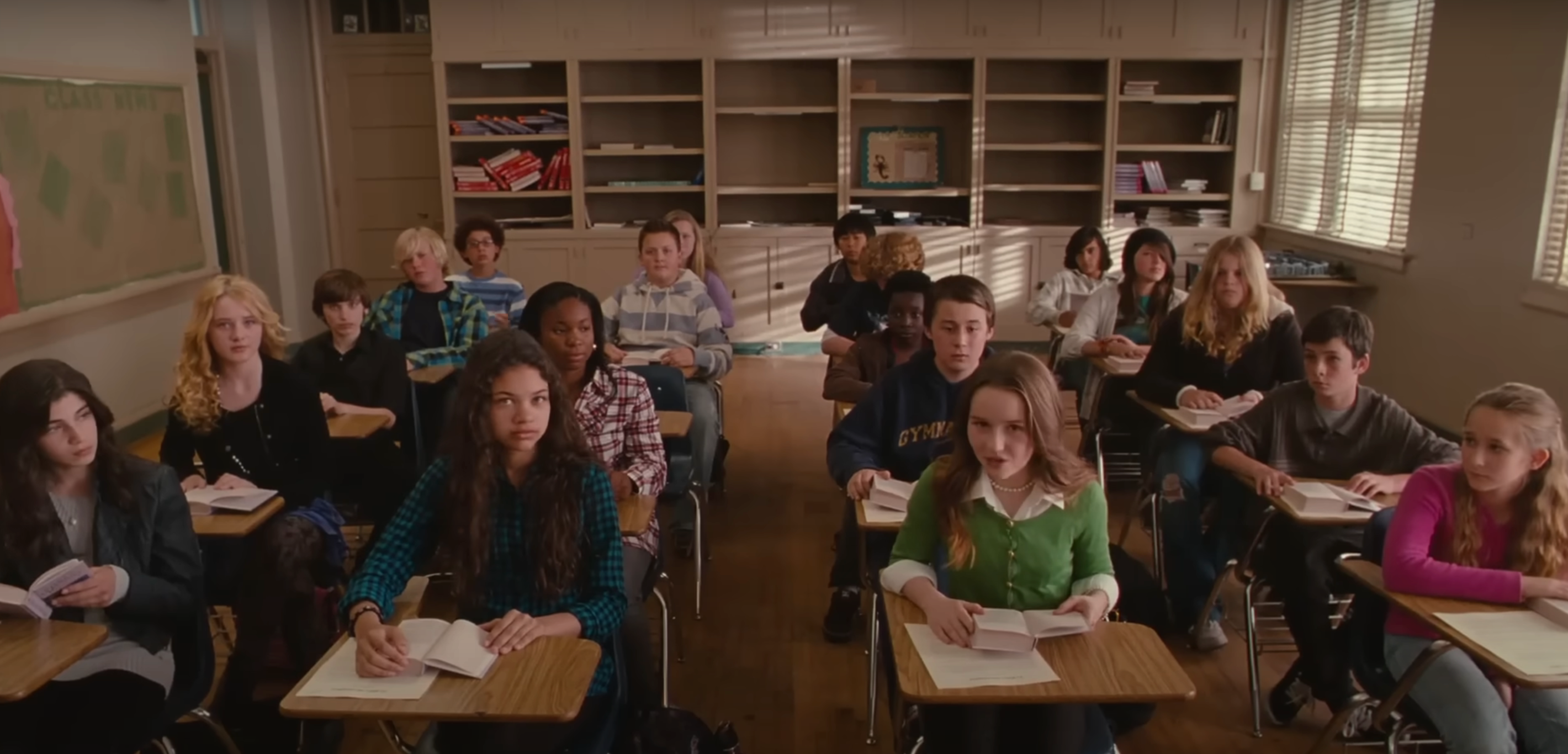 Students sitting at desks in a classroom, holding notebooks, attentively focused on the front
