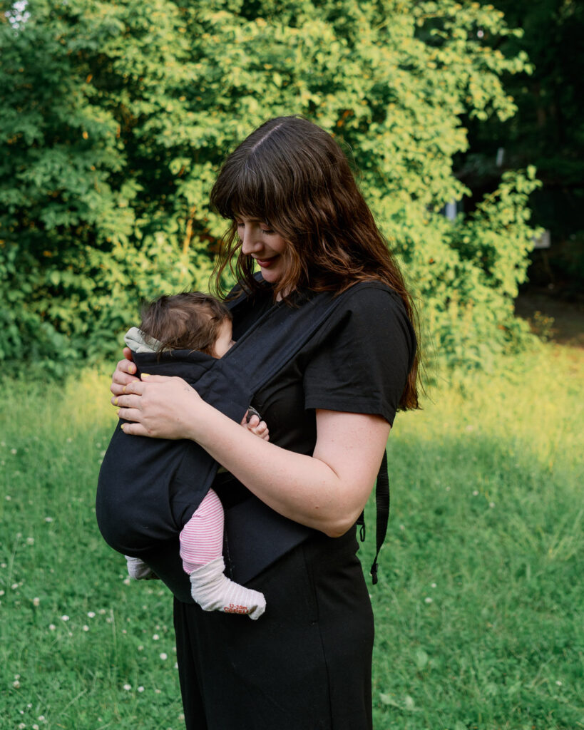 Mama mit Baby in Trage auf Wiese – gesunde Alltagsroutinen für den Mama-Alltag