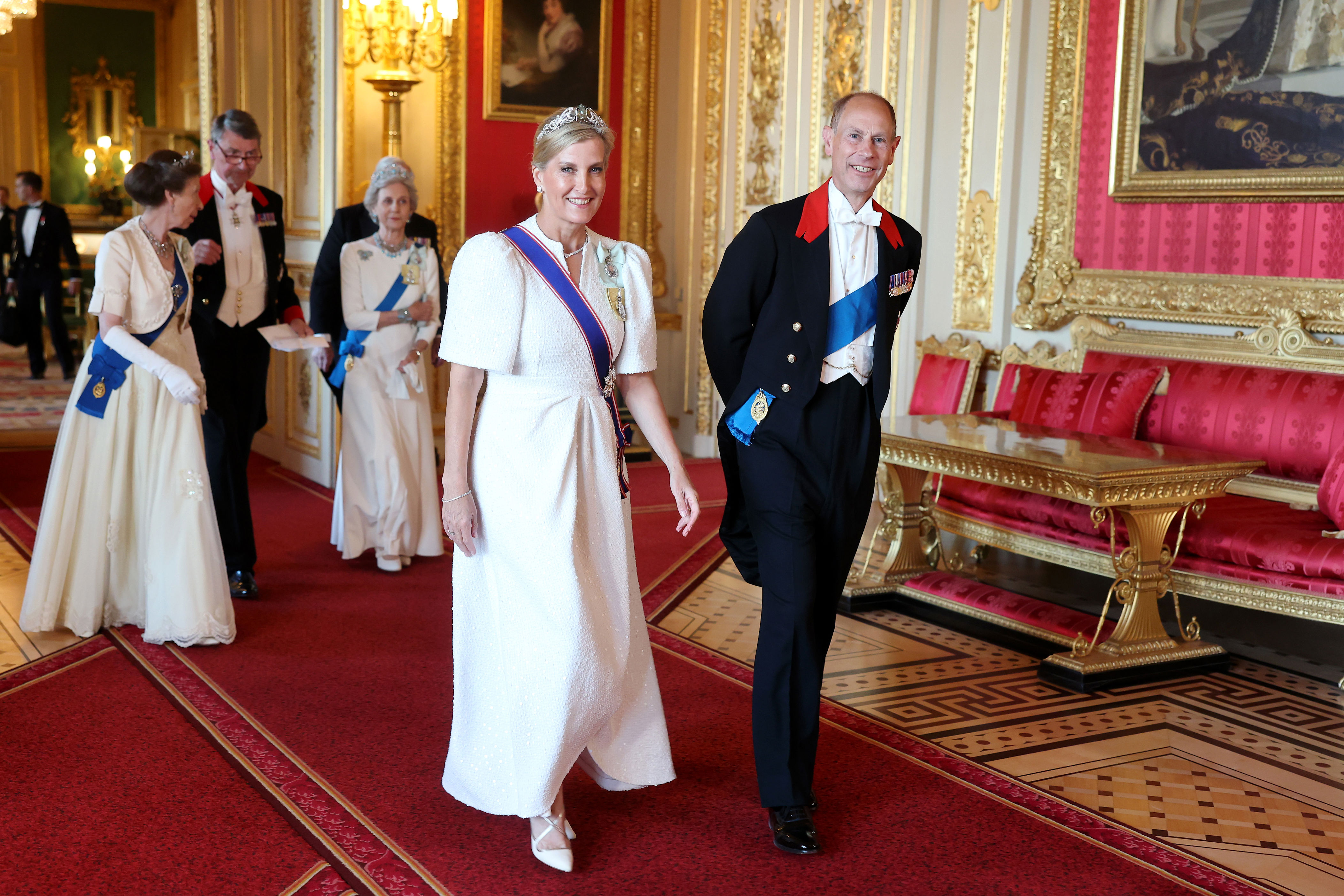 Duchess Sophie, Princess Anne, Duchess of Gloucester wearing white gowns walking with Prince Edward at a banquet
