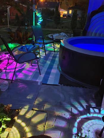 Outdoor patio with inflatable pool, chairs, and colorful light projections creating a festive atmosphere. Ideal for shopping articles on backyard decor