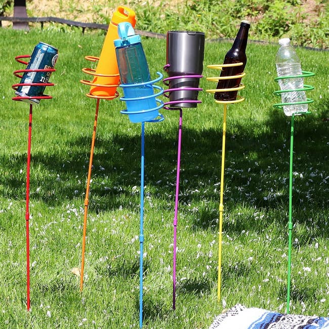 Outdoor drink holders with spiral designs hold various beverage containers on a grassy lawn