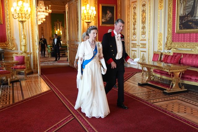 Two elderly members of the British royal family walking in an ornate room