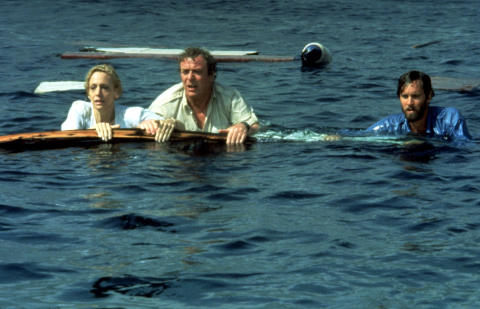 Lorraine Gary, Michael Caine, and Lance Guest floating on debris in the sea in a scene from Jaws: The Revenge