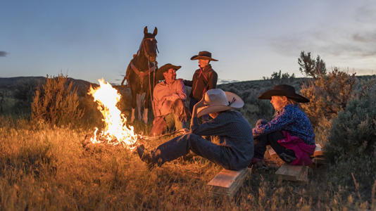 A family wearing cowboy hats with a horse around a campfire.