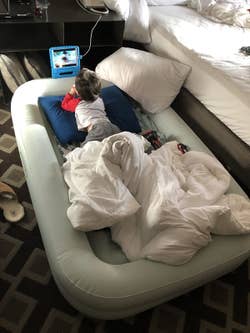 Reviewer's child watching tablet in the travel bed