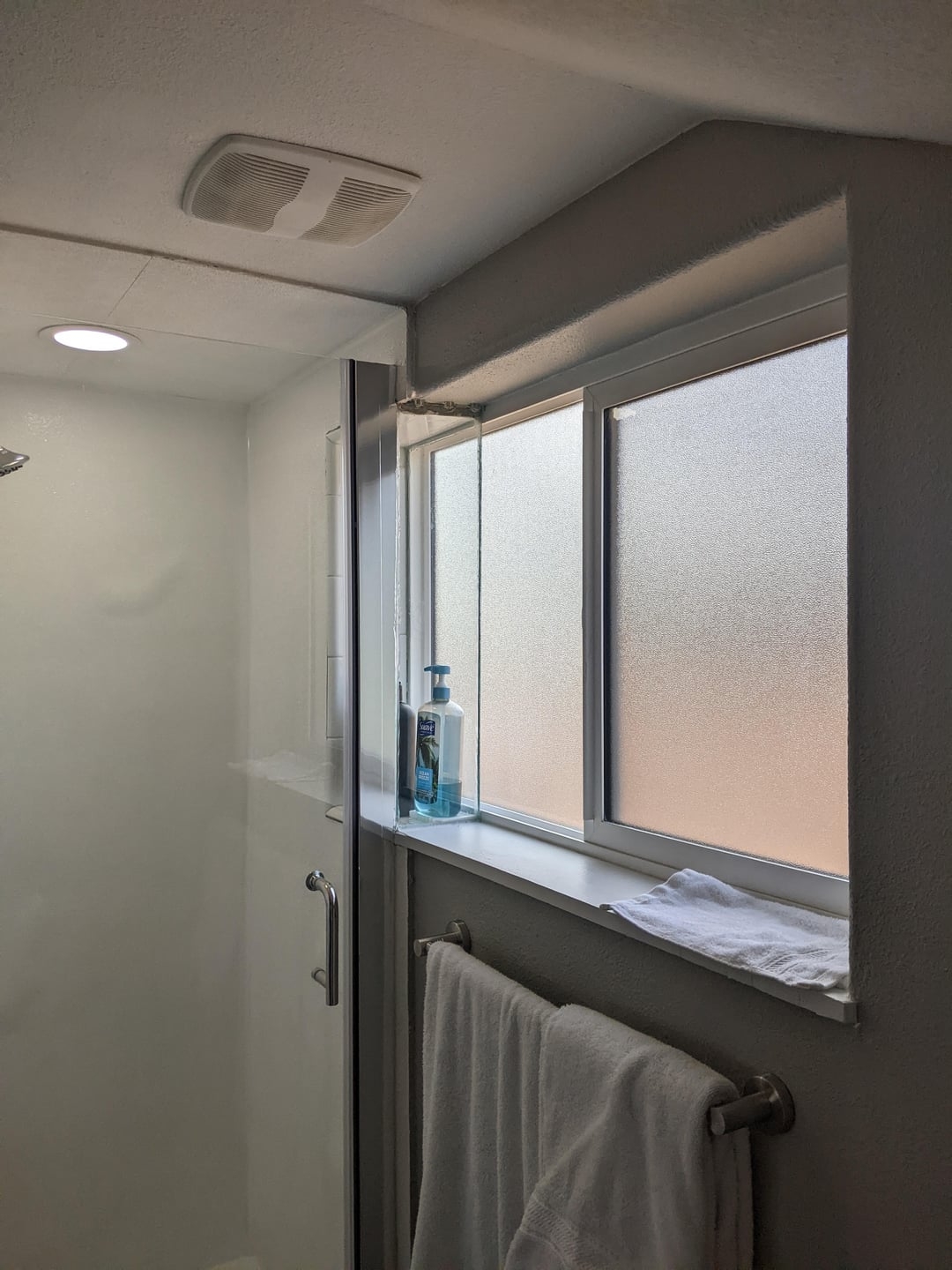 Bathroom with frosted window, glass shower door, towel rack, and soap dispenser on the windowsill, creating a clean and organized space