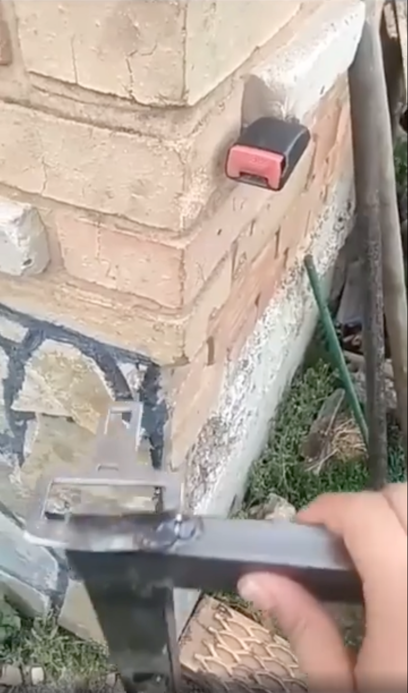 Person holds a metal bracket against a brick corner with a measuring tape clipped to the wall