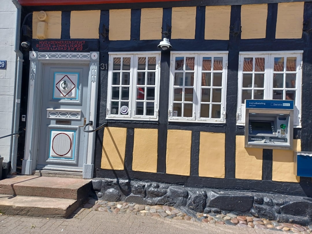 Traditional half-timbered building with ATM installed on its exterior wall. The door and windows feature decorative designs