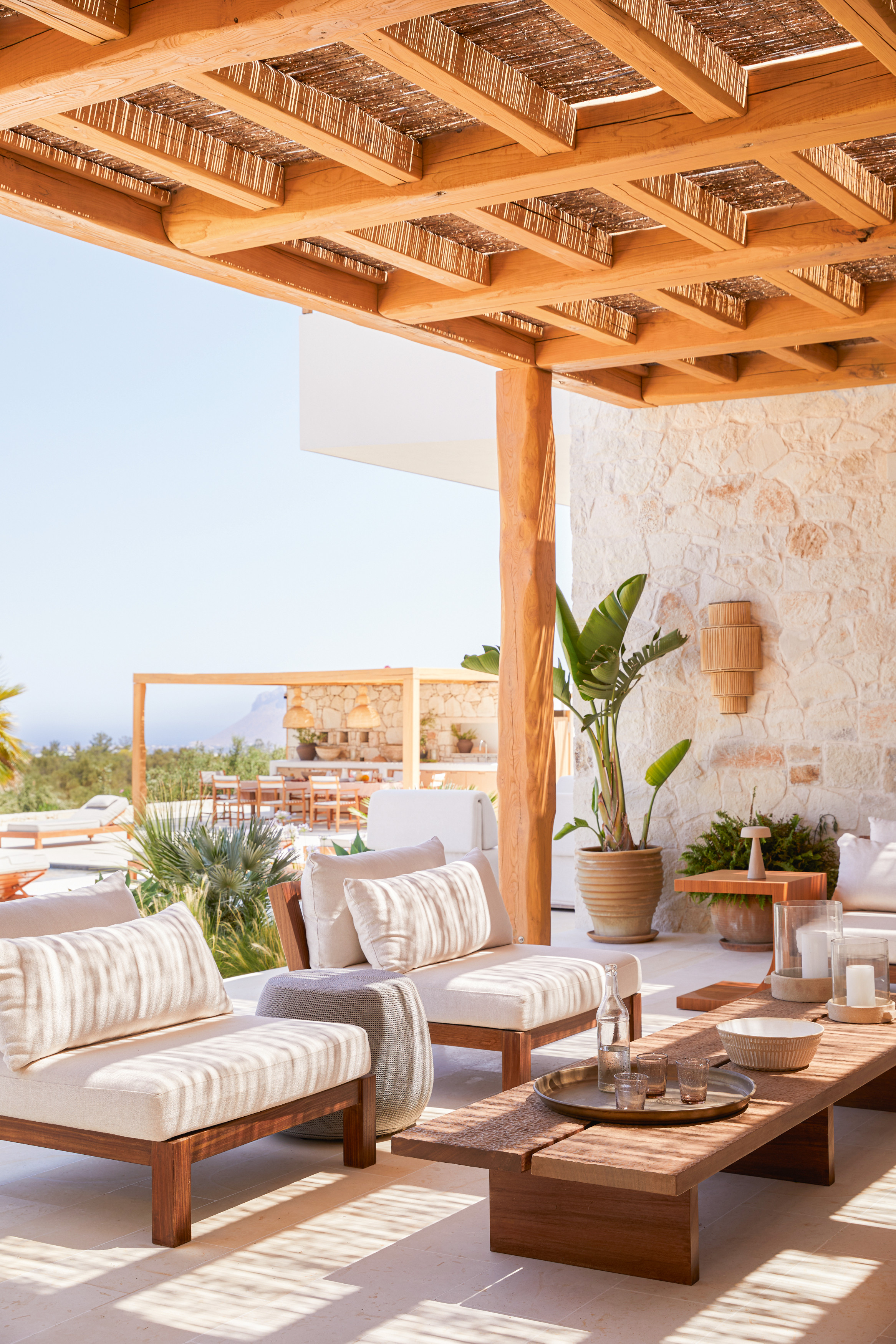 Outdoor living space in covered area with white armchairs, low wood coffee table and a palm plant