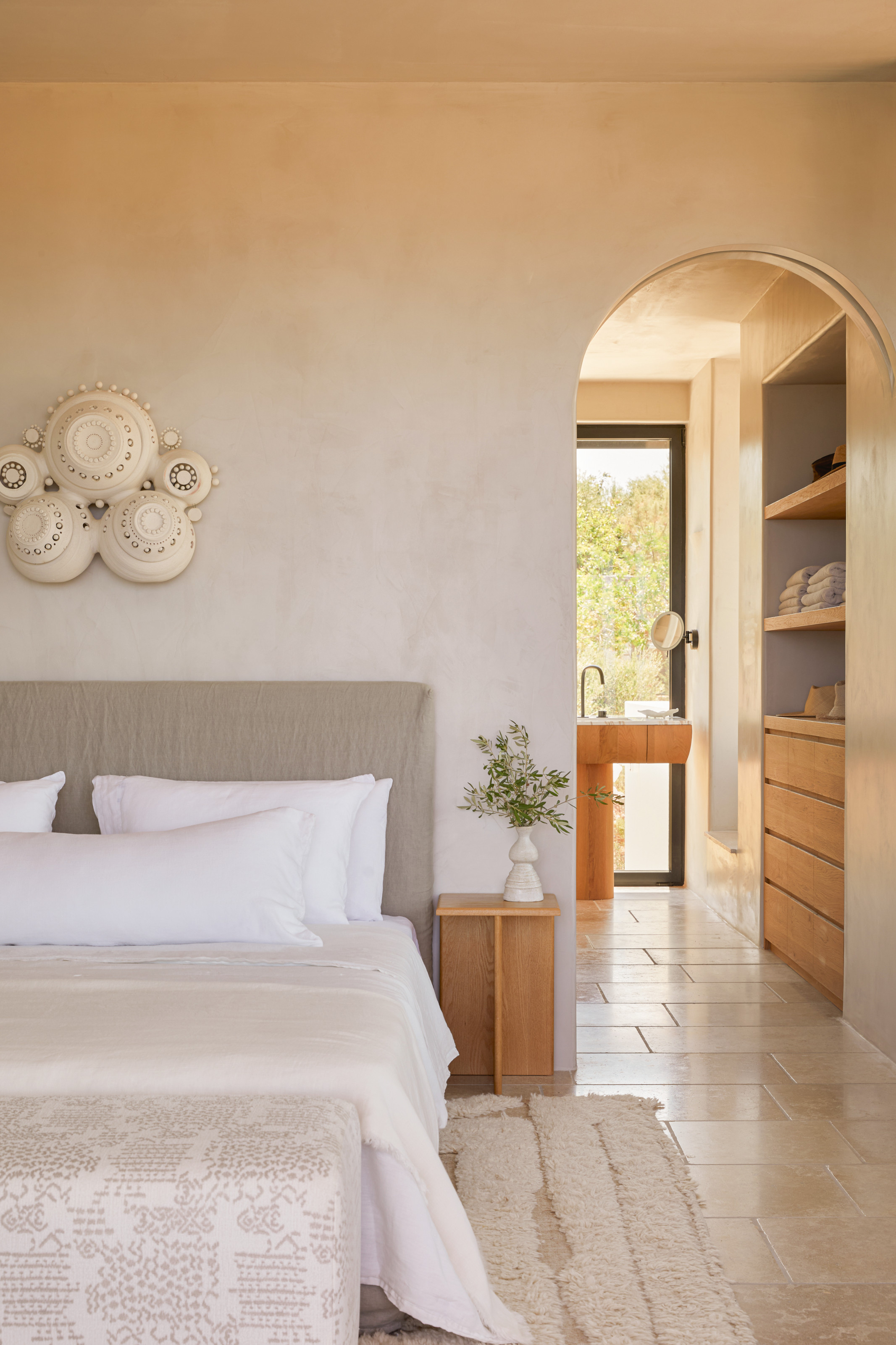 Beige bedroom with plaster-effect walls, beige upholstered headboard, ceramic artwork and white sheets