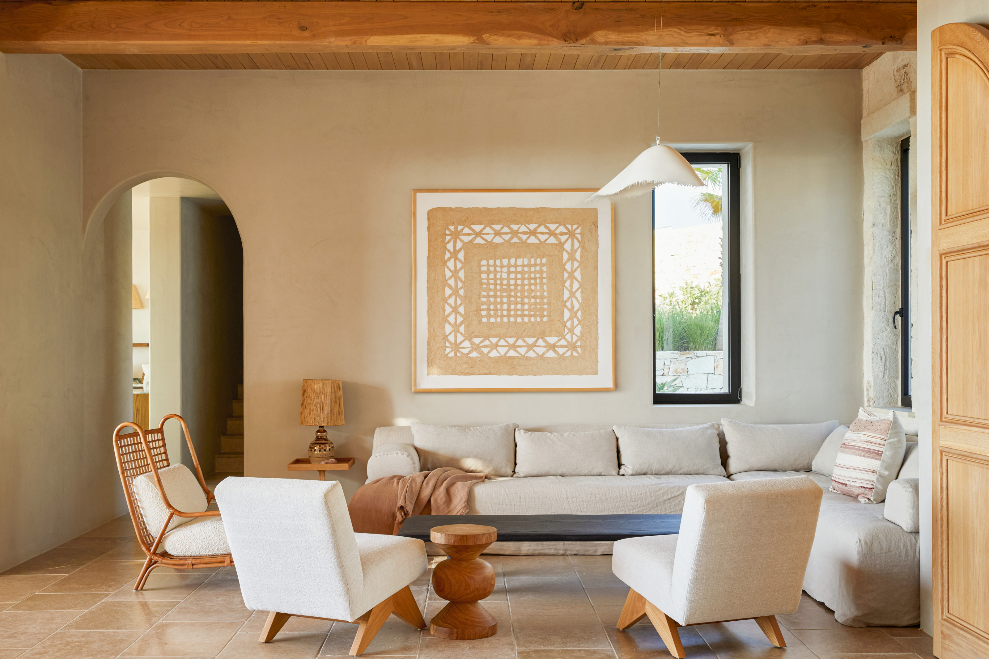 Living room with off-white armchairs and beige sofa, wicker accent chair, beige patterned artwork and white pendant light