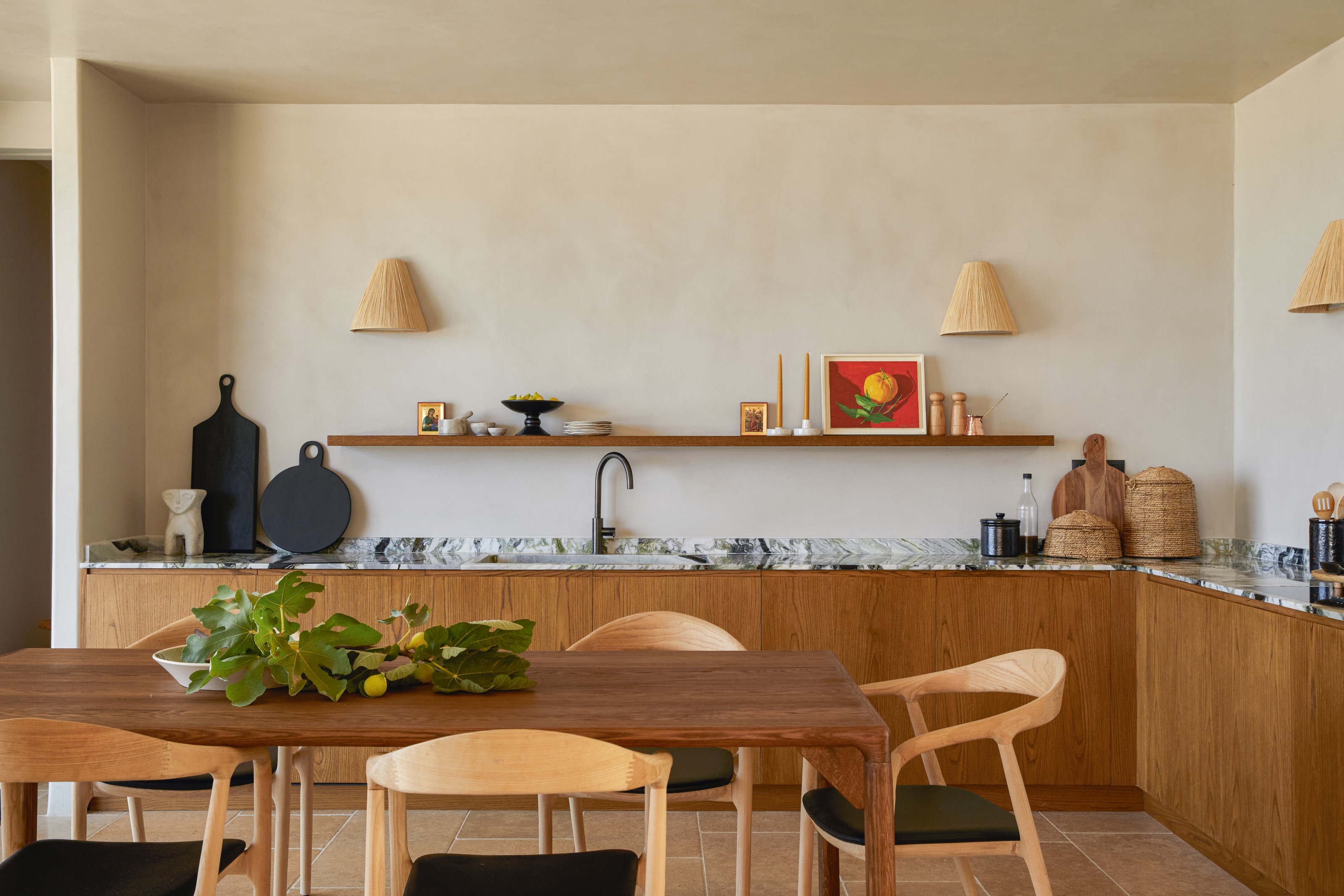 Natural wood kitchen with black and white stone countertop, plaster-effect walls, straw wall lightshades, open shelving, and a wooden dining table and chairs