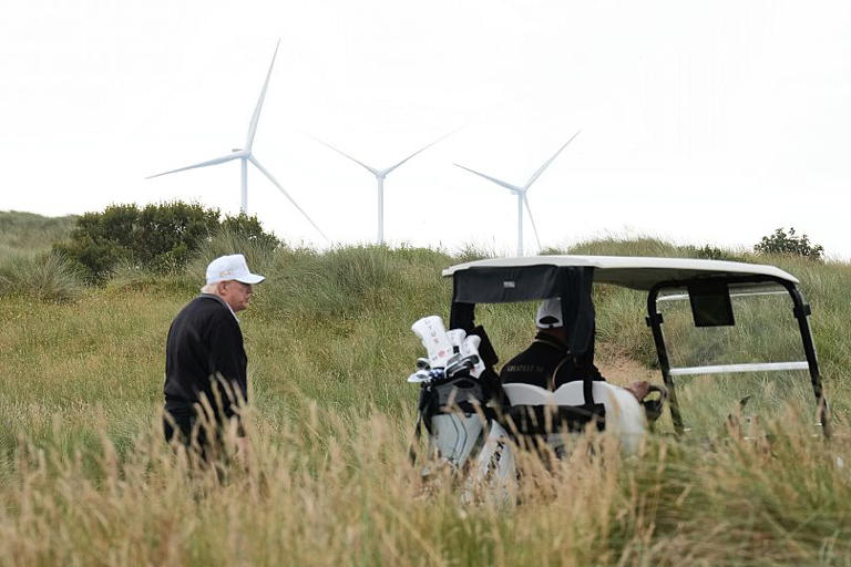 Il presidente Donald Trump cammina sullo sfondo di turbine eoliche durante la cerimonia di inaugurazione del campo da golf Trump International Golf Links, vicino ad Aberdeen, AP Photo/Jacquelyn Martin