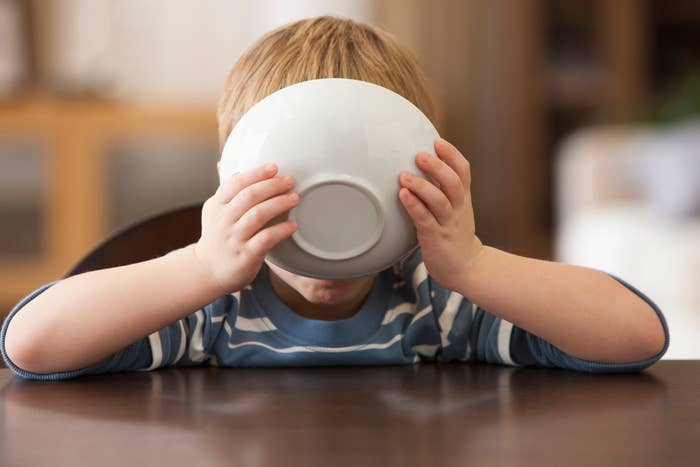 Child in striped shirt drinking from a large bowl at a table, covering their face