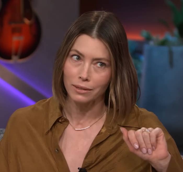 Jessica Biel with short hair wearing a casual collared shirt gestures during an interview on a talk show