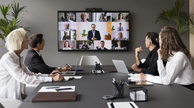 People in conference room with online meeting on screen