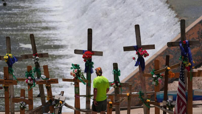 A man walks past crosses and flowers that form a make-shift memorial along the Guadalupe River as the Texas Senate and House Select Committees on Disaster Preparedness and Flooding hold a public hearing in Kerrville, Texas, Thursday, July 31, 2025.