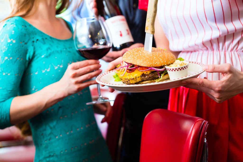 Friends or couple eating fast food in American fast food diner, the waitress serving the food, burgers, fries, and red wine