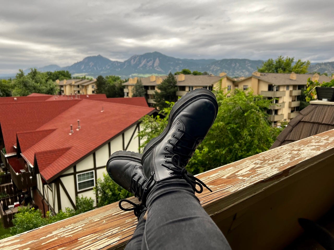 Person wearing boots with feet on ledge overlooking mountains, rooftops