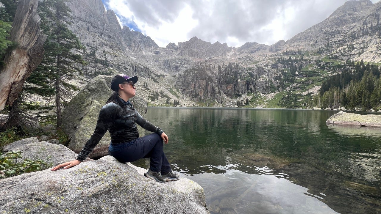 Author Emily Pennington sitting on rock near water in front of mountains