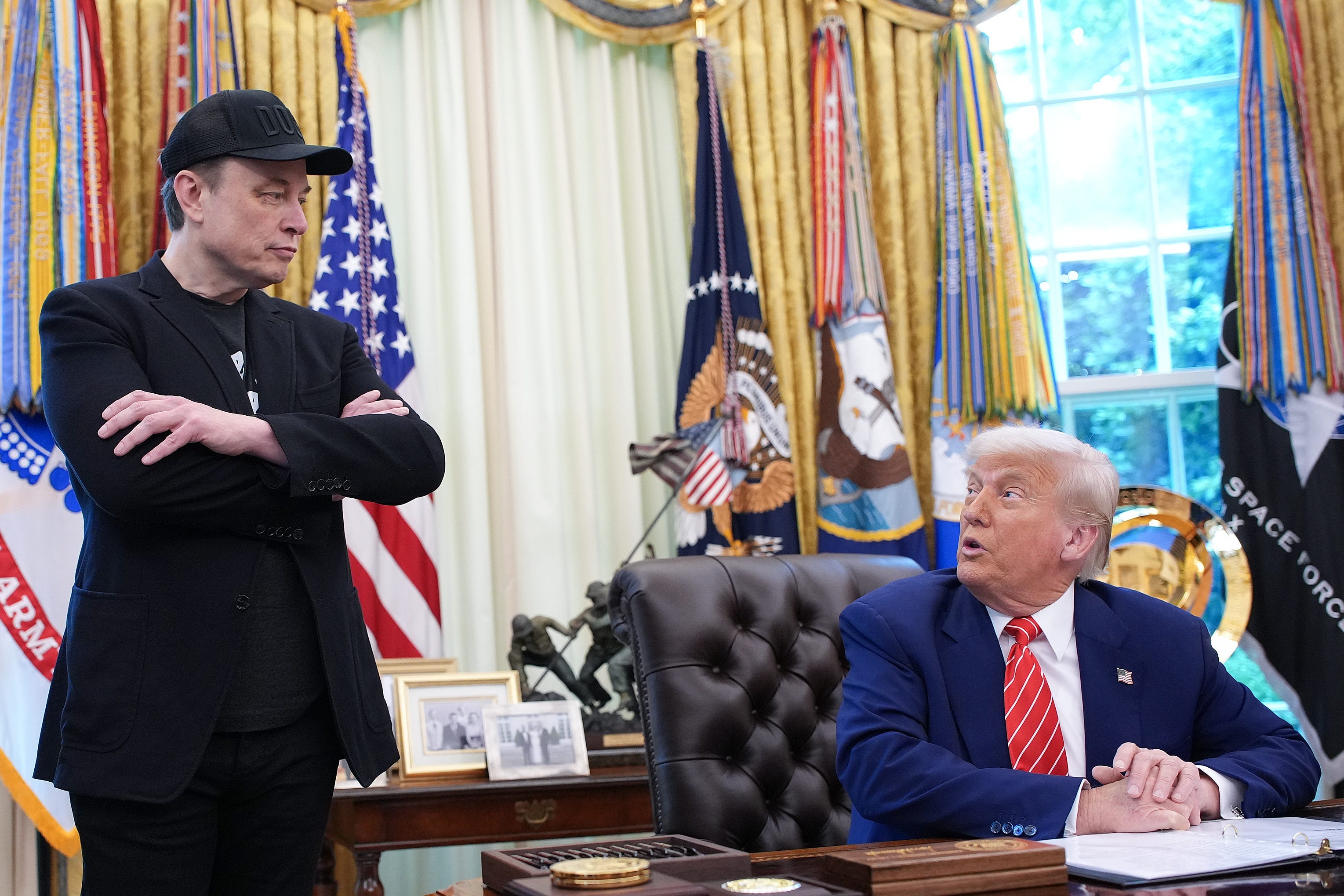 Elon Musk looking at President Donald Trump in the Oval Office.