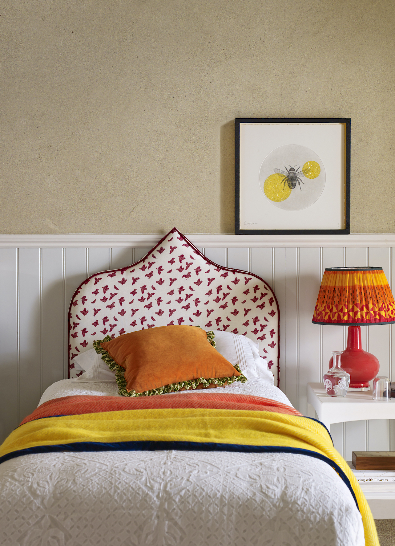 teen bedroom idea with upholstered headboard, bright orange and red table lamp, shiplap wall halfway up, textured wallpaper.Orange and red accents, bee artwork, white bedside
