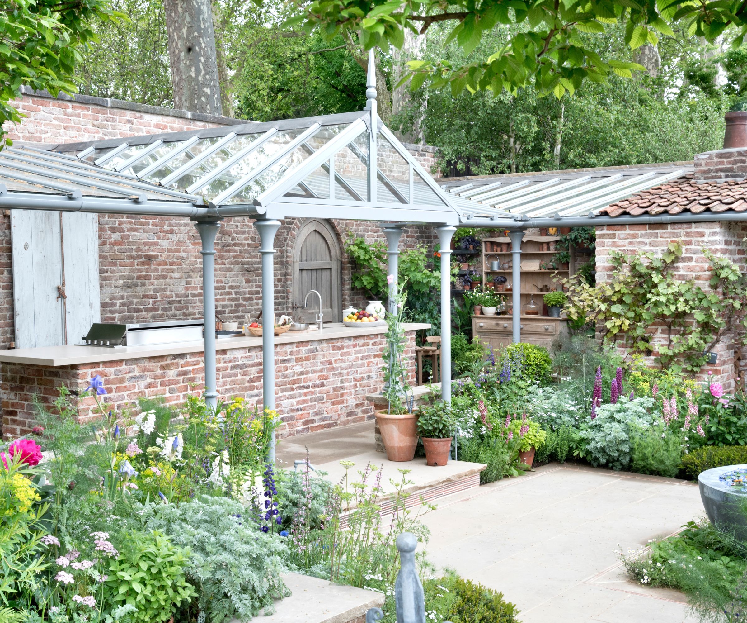outdoor kitchen built into a walled garden with a green house roof over the top