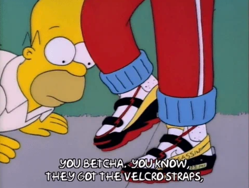 Cartoon character kneels, admiring another's flashy sneakers with Velcro straps. Caption: