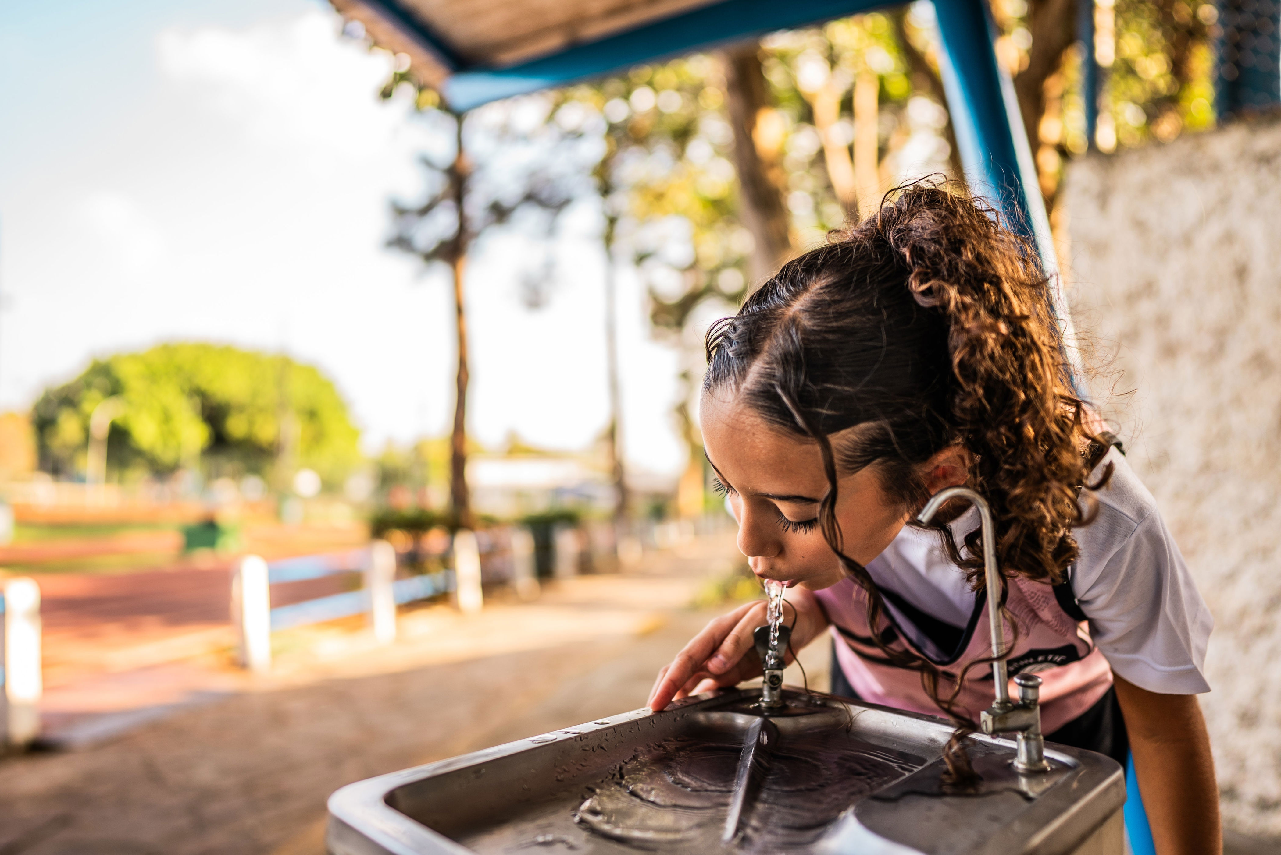 Person drinking water from an outdoor fountain, with a blurred park background