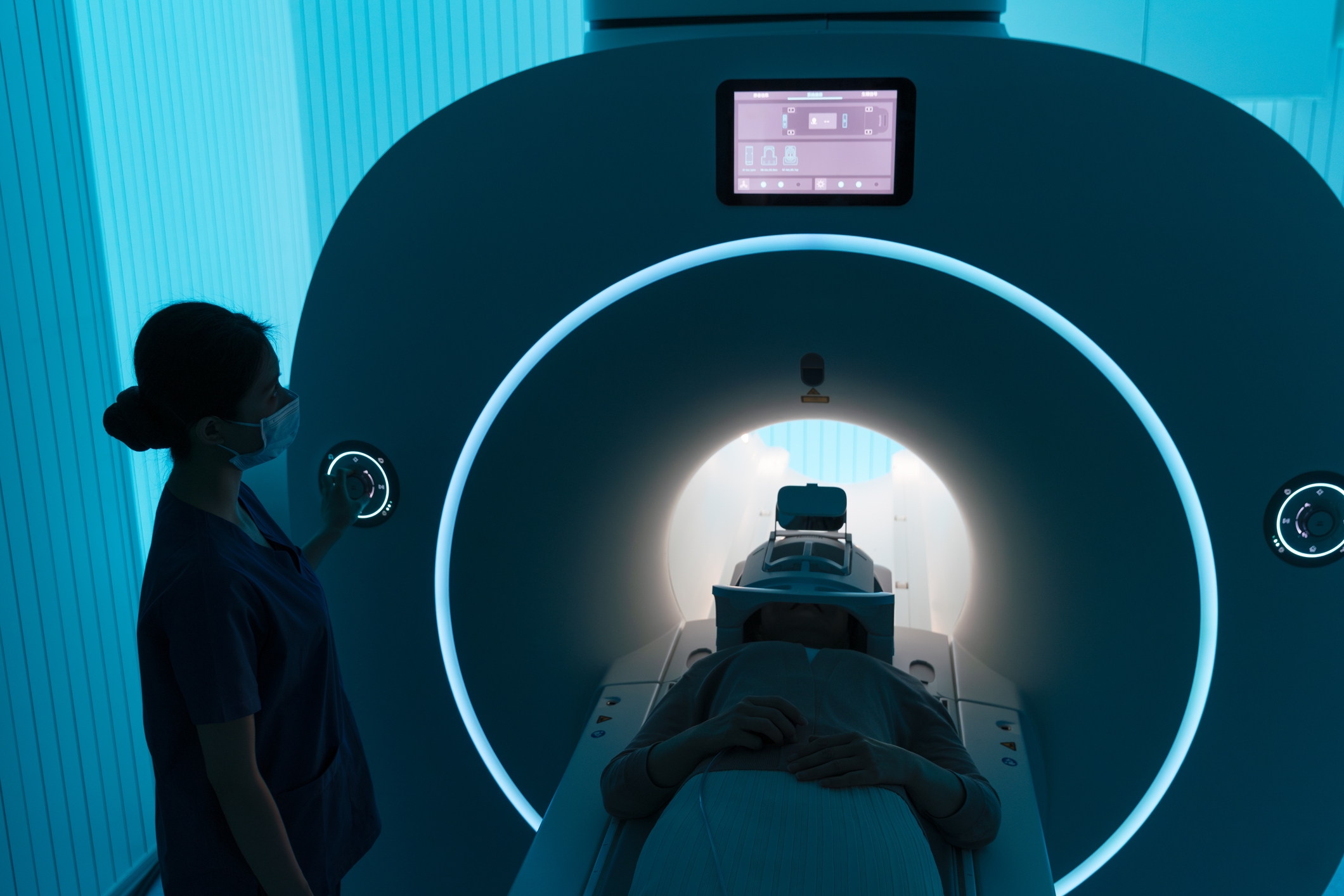 A person in an MRI machine with a medical staff member nearby in a dimly lit room