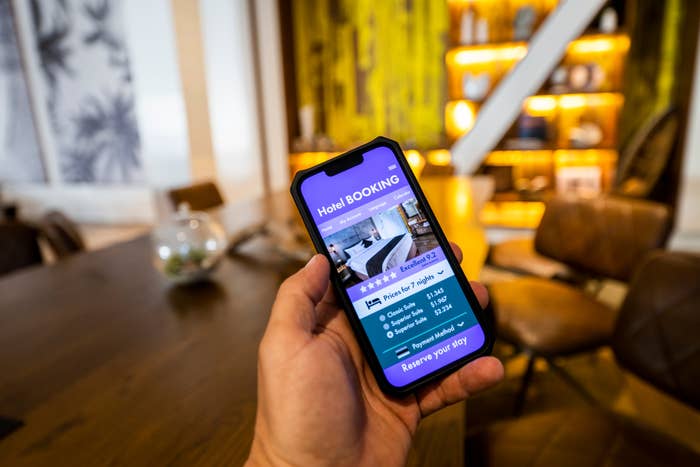 Person holding a smartphone displaying a hotel booking app interface in a cozy, modern room
