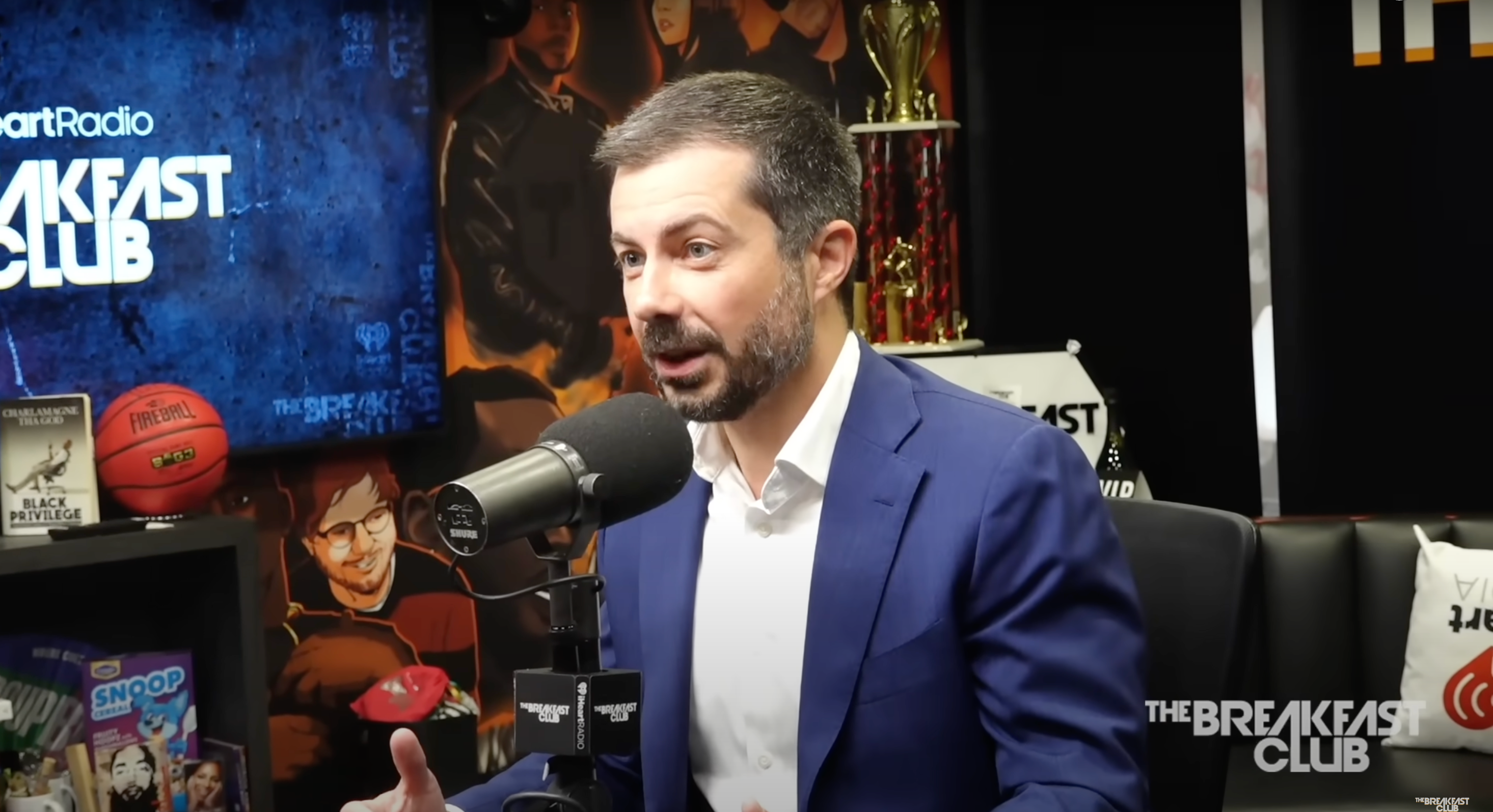 Person in a blue suit speaking into a microphone on a radio show with trophies and posters in the background