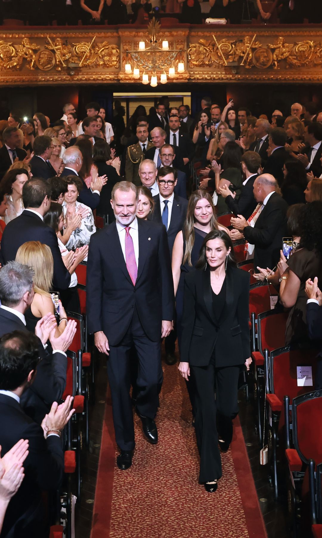 La Familia Real a su llegada al Liceo, donde tuvo lugar la ceremonia de entrega de los Premios Princesa de Girona, el 23 de julio. . La Reina, que peinó su melena con ondas, vestía de Mango y llevaba unos pendientes con hilos de Tous y zapatos "babies" de Sézane