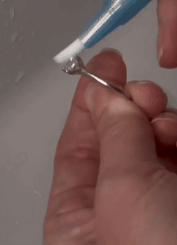 A hand uses a toothbrush to clean a silver ring, demonstrating jewelry cleaning at home