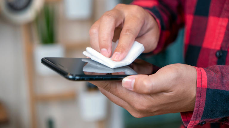 Man in red and black flannel wiping smartphone screen with white cloth
