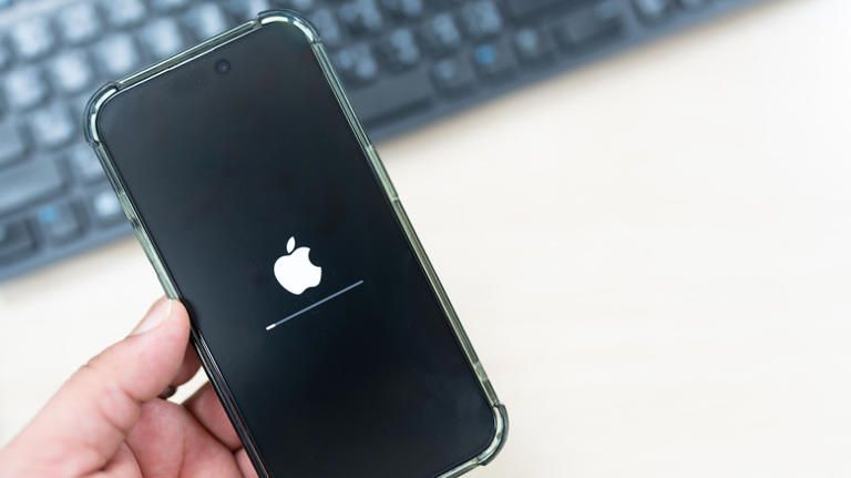 Left hand holding rebooting iPhone with black keyboard in blurred background