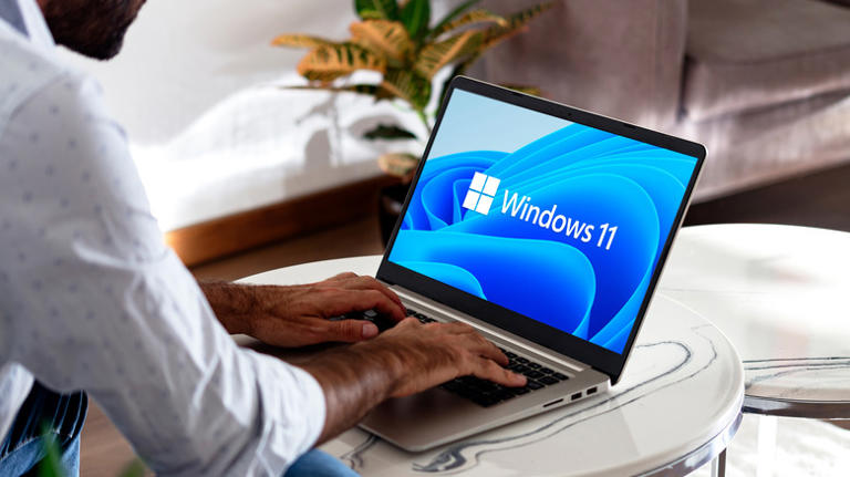 A man places his hands on the keyboard of a laptop with Windows 11 logo on the screen.