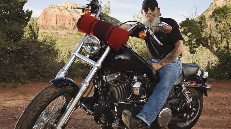 ﻿A biker sits on a black motorcycle with a red blanket fastened to the front