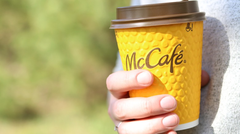 A hand holds a yellow, paper cup of McDonald's coffee outside