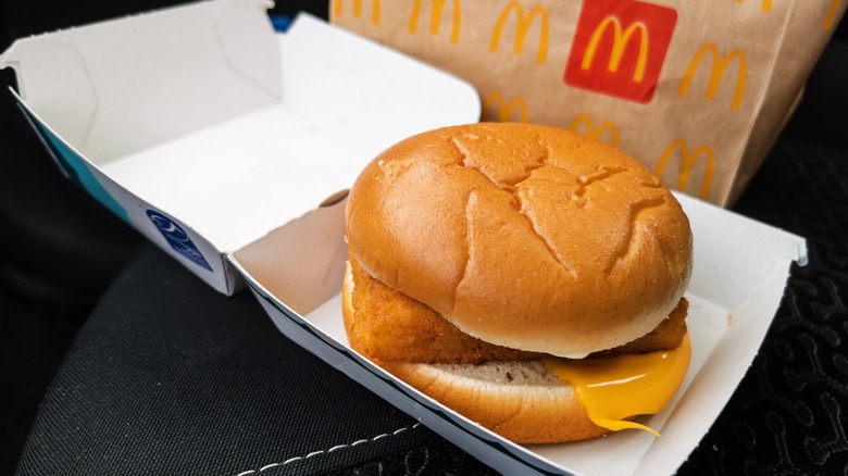 A Filet O' Fish in a cardboard box next to a McDonald's bag
