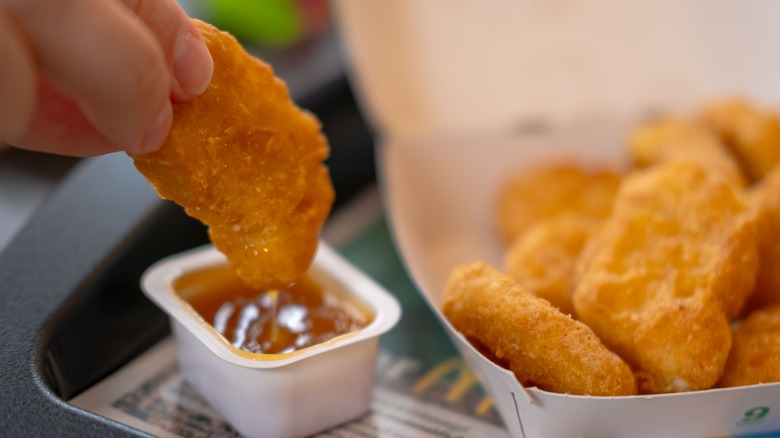 A close-up of a hand dipping a McNugget into brown sauce