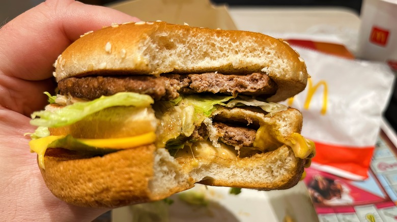 A hand holds a McDonald's Big Mac with a bite taken out