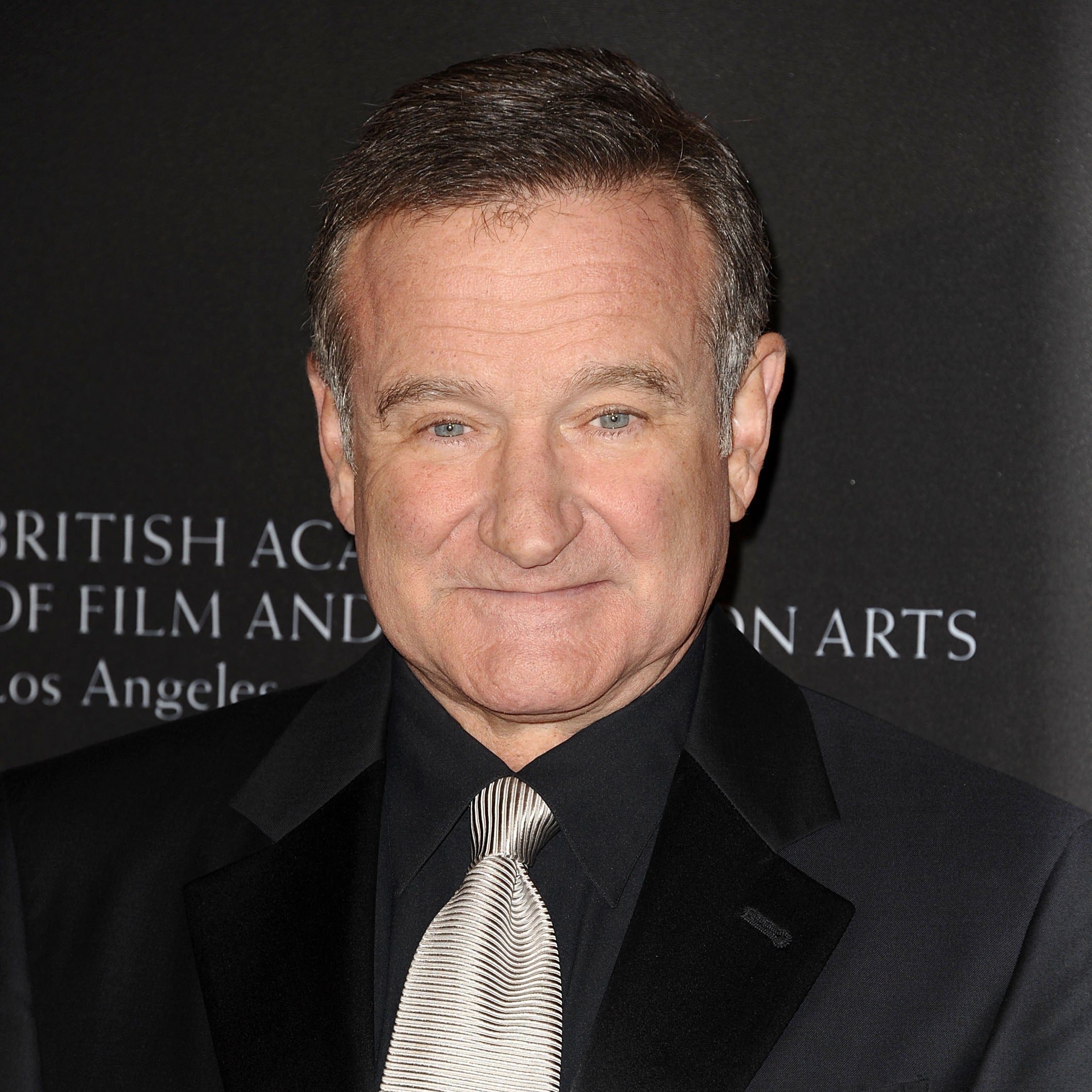 A person in a formal black suit and tie poses against a backdrop related to film and television arts, attending an event