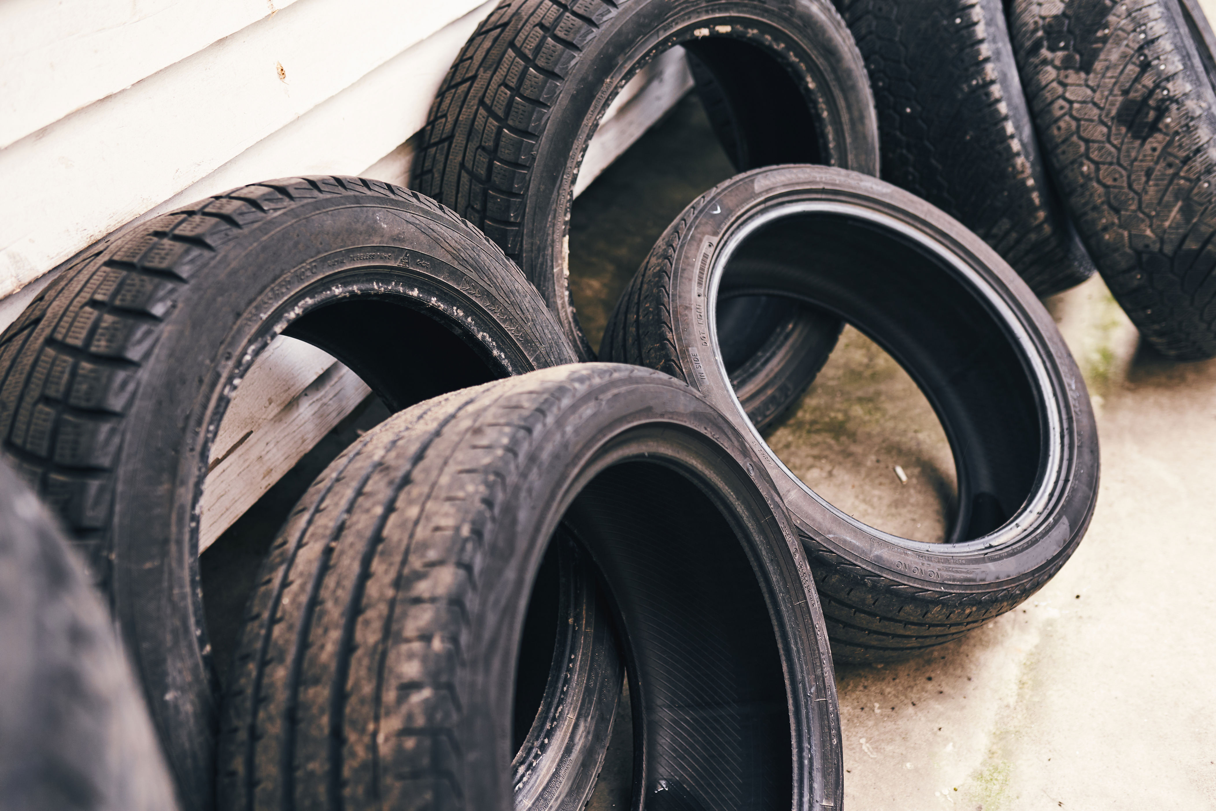 Several tires are leaned against a wall in an outdoor setting