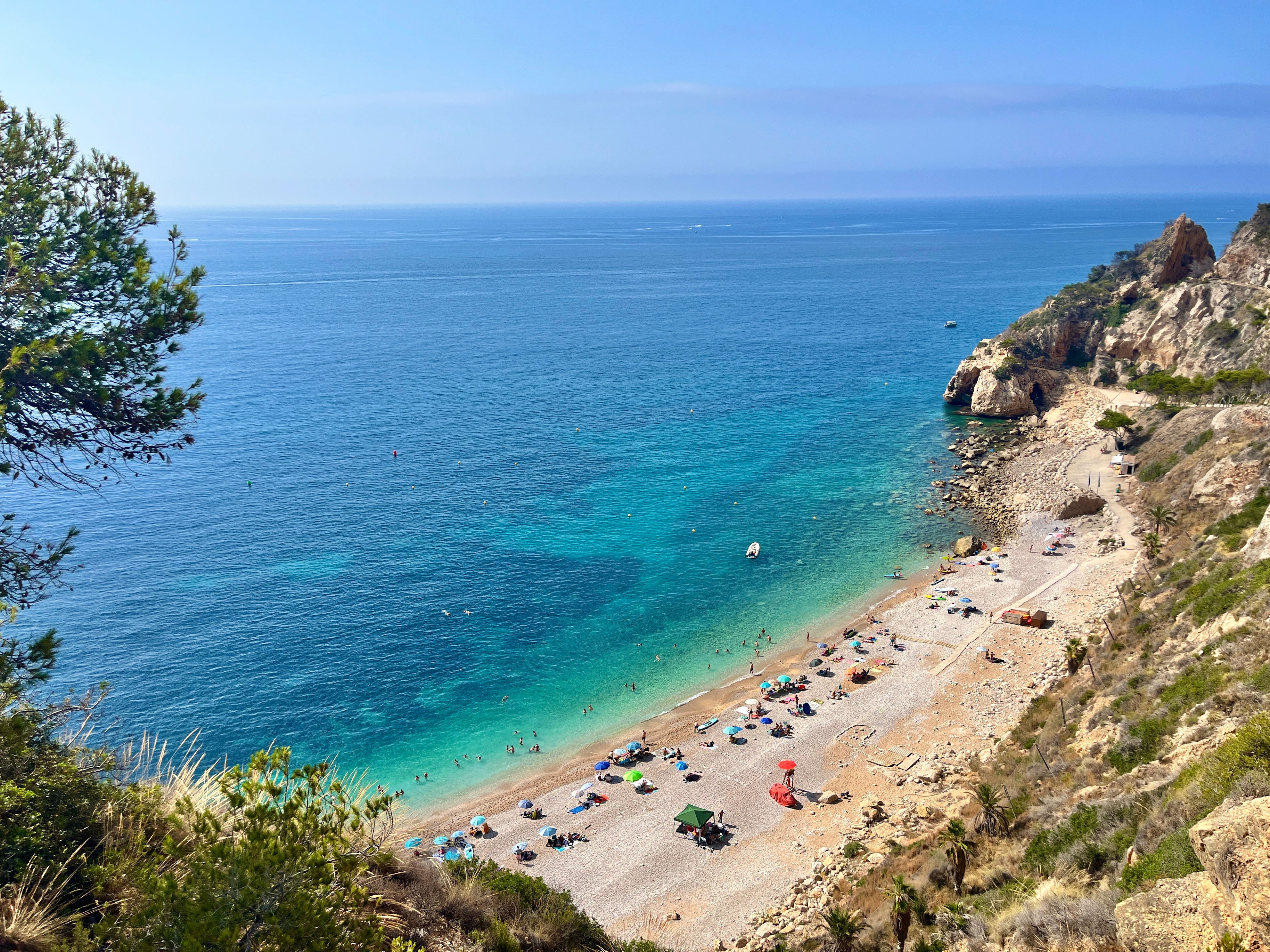 View of a scenic beach with people sunbathing and swimming, bordered by cliffs and clear ocean water