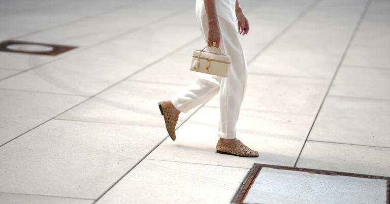 Model wears a white blouse, white baggy trousers, brown wicker shoes and beige mini leather handbag, all from Loro Piana's Summer collection, on July 1, 2025 in Munich, Germany.